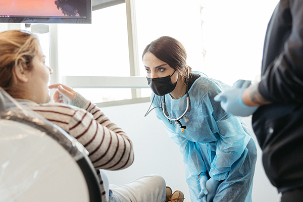 A female dentist in a mask and protective gear consults with a patient in a dental clinic.
