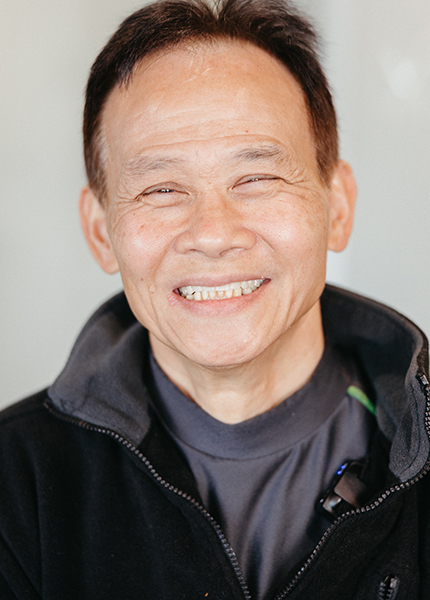 Portrait of an elderly Asian man with whole mouth dental implants, smiling at the camera, wearing a dark jacket. His hair is black with hints of gray.