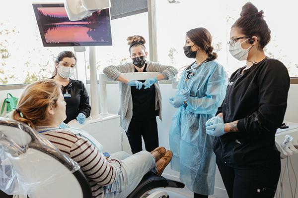 Dental team in protective gear discussing whole mouth dental implants with a female patient in a dentist's office.