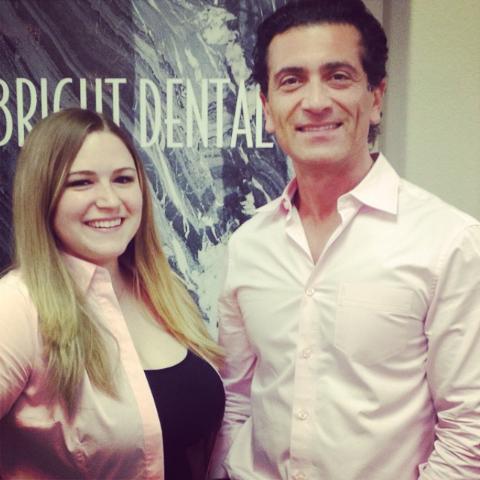 Two smiling adults, a man and a woman, standing in front of a sign that reads "rubricut dental." both are wearing pink shirts.